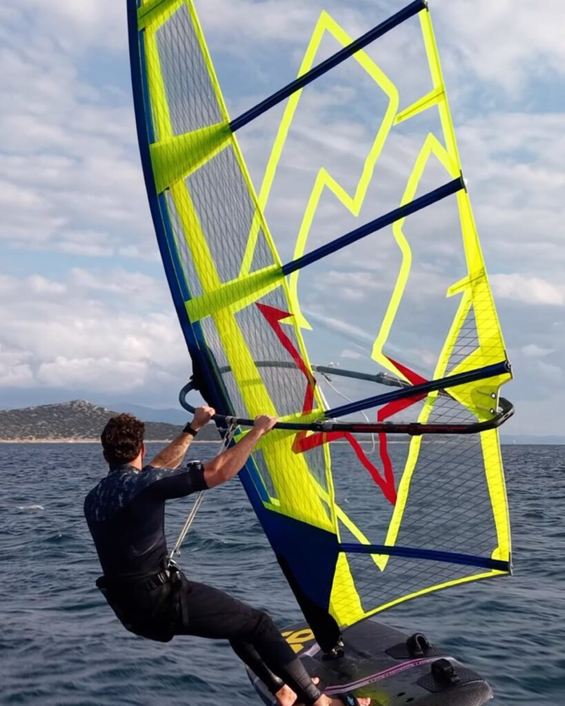 Windsurf foiler powering up a fluo yellow CHS Challenger AeroFoil sail off a rocky coast