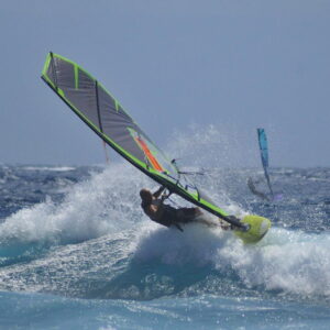 CHS GS4 all-round wave sail in grey and fluo green, windsurfer carving a bottom turn on a breaking wave
