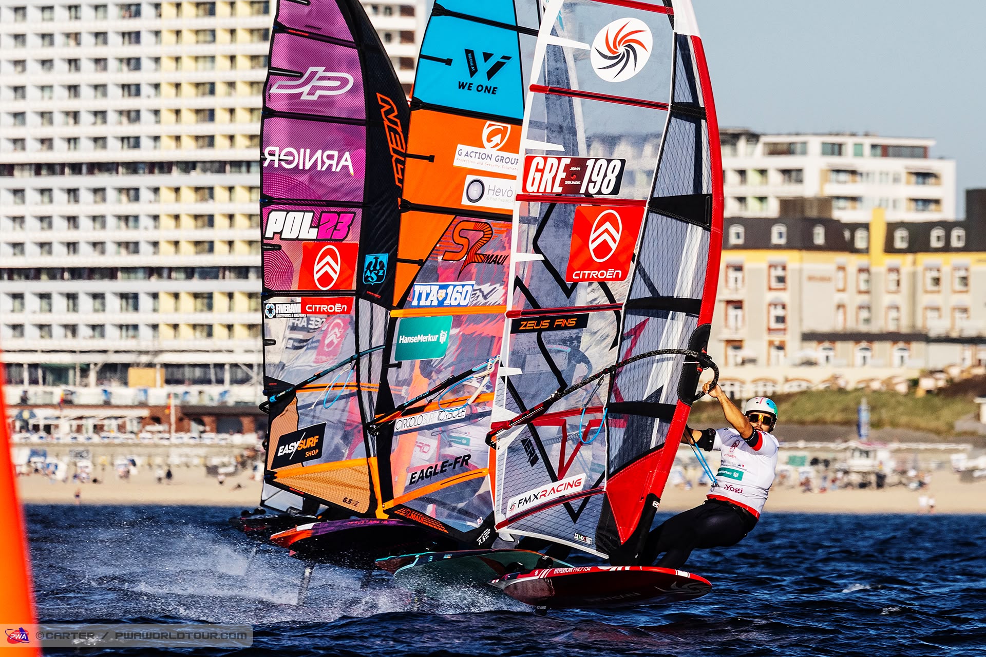 Foil slalom riders racing off the Westerland seafront at the PWA World Cup Sylt 2026, with John Soukos GRE-198 on the right